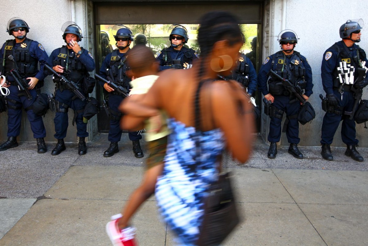 A woman carries a child along West Roadway in front of a wall lined with heavily armed California Highway Patrol. Officers from around the country came to Cleveland to reinforce the police presence at the Republican National Convention. (July 19, 2016)